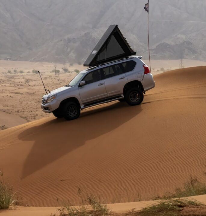 A white suv with a tent on top of a sand dune.