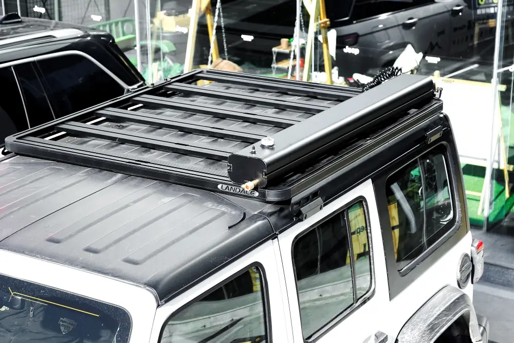 MG_2774.jpg A white SUV with a black roof rack features the Road Shower and an awning on top, parked indoors. Other vehicles and a green area with chairs can be seen in the background.