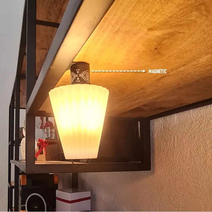 Slide3-1-1.jpg A soft, warm light from the magnetically attached Lamp Shade with a fluted frosted design illuminates the area under a wooden shelf. The shelf, held up by metal framing, supports various objects beneath it.