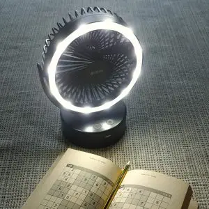 A compact Fan with LED Light rests on a gray textured surface. In front, an open puzzle book displays a Sudoku grid, ideal for a brain-challenging break.