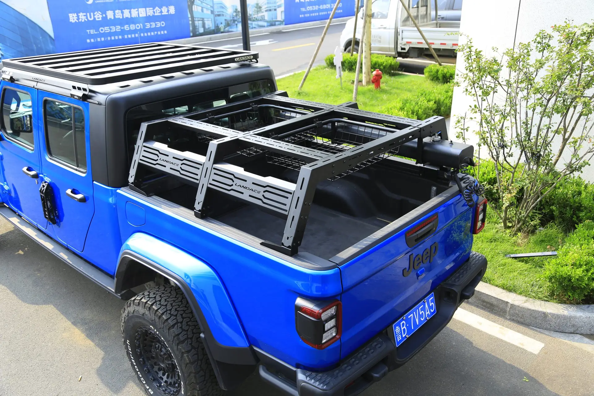 bedrack_top_! A bright blue Jeep Gladiator with a black roof rack and a Chicari Bed Rack installed in the truck bed, parked on a city street near greenery and buildings.