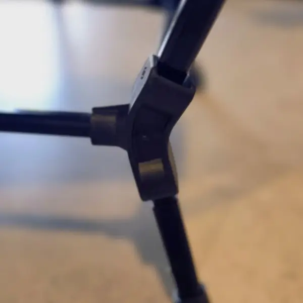 chicari chillax chair (3) Close-up of a black plastic joint connecting the legs of the Chicari Chillax Chair, a folding director’s chair, set against a blurred, neutral background.