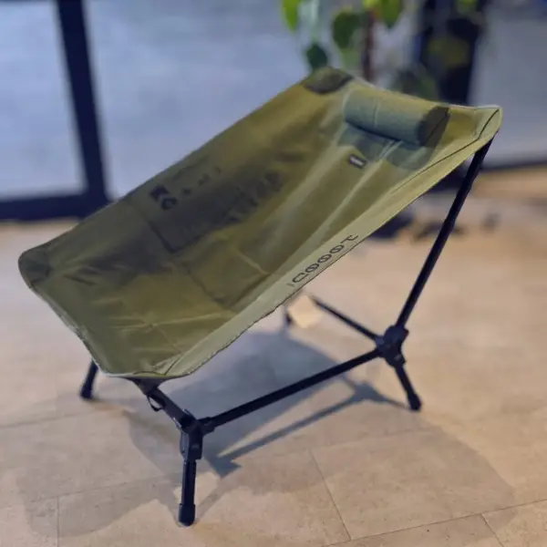 chicari chillax chair (9) The Chicari Chillax Chair in green fabric, featuring a headrest and black metal frame, is set on a light indoor floor, with a leafy plant blurred in the background.