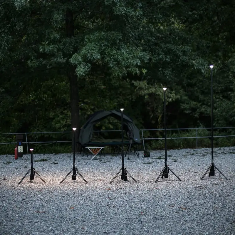 finel_camping_VIP_._._._N7_1_b4d72bd3-d240-4770-abe7-730ede4a850a Six Finel N7 tripod camping lights with shades are arranged on gravel in front of a tent, surrounded by trees and greenery, creating a romantically illuminated outdoor campsite scene.